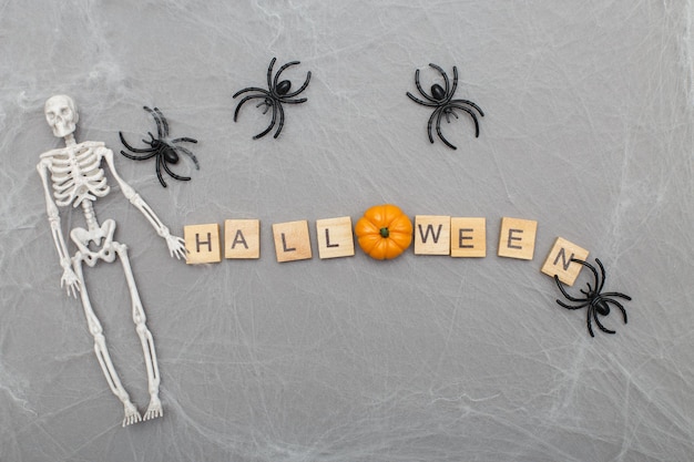 L'inscription halloween avec toile d'araignée et araignées sur fond gris avec un squelette