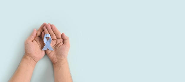 Inscription à la journée mondiale du diabète. Ruban bleu dans les mains de l'homme sur fond bleu. 14 novembre. Novembre Sensibilisation à la santé des hommes, Novembre Bleu. Espace de copie. Bannière vue de dessus.