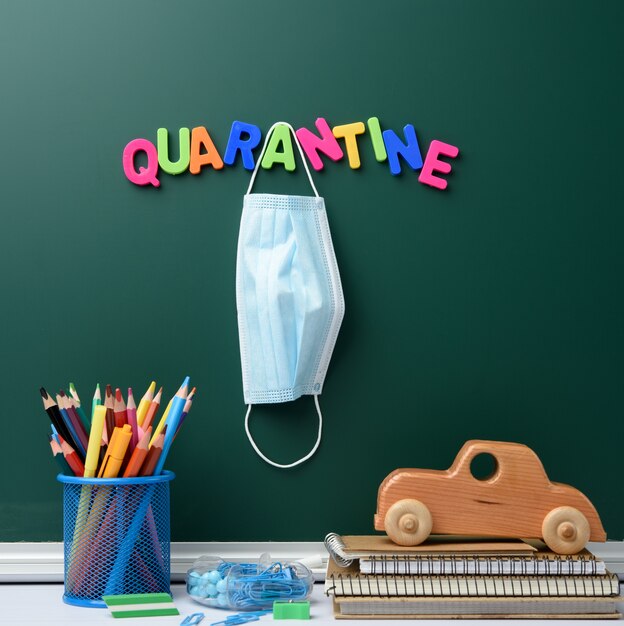 Inscription de quarantaine à partir d'une lettre en plastique multicolore sur un tableau de craie verte, masque médical jetable suspendu