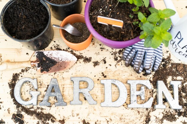 Inscrivez JARDIN en lettres métalliques autour de la terre renversée et des pots de plantation sur une table de jardin en bois.