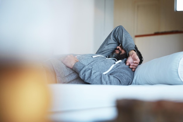 Insomnie fatiguée et un homme stressé sur un lit souffrant d'épuisement professionnel triste et de problème de santé mentale Dépression de fatigue et une personne dormant dans la chambre d'une maison alors qu'elle est déprimée ou malade avec une gueule de bois