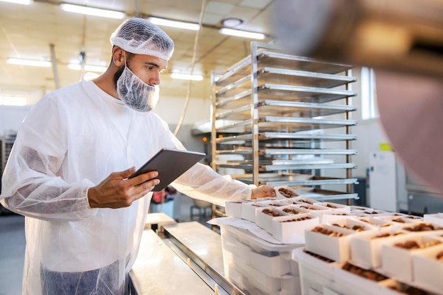 Un inspecteur des aliments en uniforme blanc stérile tient la tablette et regarde les biscuits collectés Le contrôle des aliments est important si nous voulons des aliments sains et de qualité