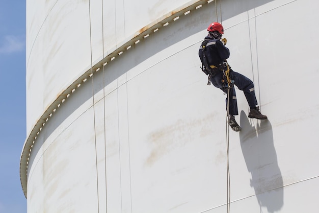 Inspection de l'accès à la corde du travailleur masculin de l'huile de l'industrie de l'ombre du réservoir de stockage blanc d'épaisseur