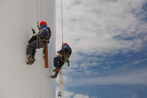 Inspection de l'accès par corde du réservoir de hauteur inférieure de deux travailleurs masculins de l'épaisseur du réservoir de stockage de la plaque de coque