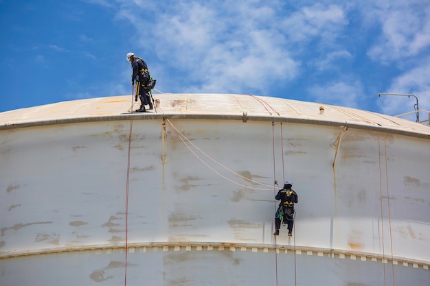 Inspection de deux travailleurs masculins portant la première corde de sécurité du harnais de sécurité travaillant à un endroit élevé sur le toit du réservoir sphérique