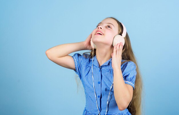 Inspiré par la musique Petit enfant écoutant de la musique Enfant mignon avec un casque fond bleu Petite fille portant un casque stéréo Enfant utilisant la technologie pour les loisirs ou l'éducation Casque moderne