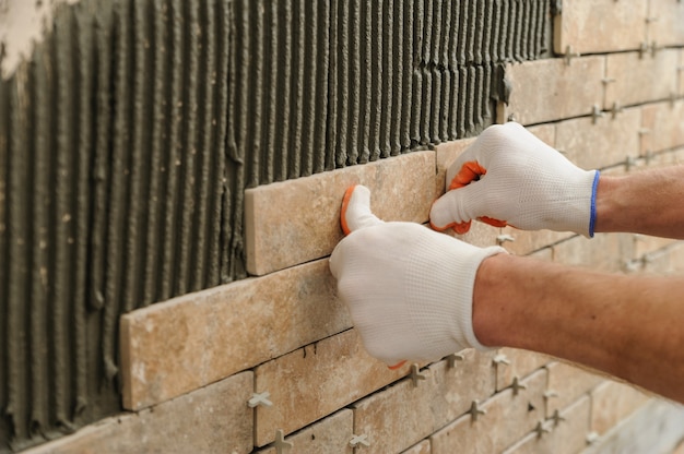 Installation des carreaux sur le mur. Un ouvrier mettant des tuiles sous forme de brique.