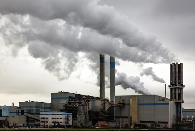 Une installation industrielle avec des tuyaux d'échappement d'où une épaisse fumée sort dans le ciel nuageux