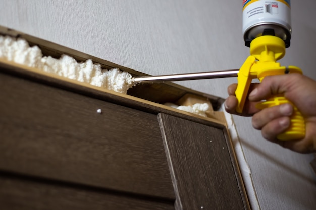 Installation de portes dans la maison. Le maître mousse les espaces entre la porte et le mur avec de la mousse de polyuréthane.