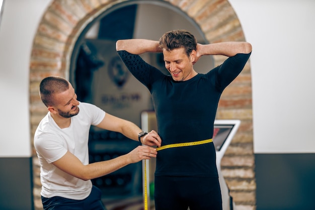 Instructeur de conditionnement physique mesurant la taille de l'homme mûr avant de s'entraîner dans la salle de sport.