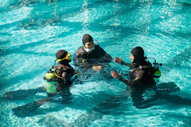 Instructeur et deux plongeurs en aqualungs, cours de plongée en école de plongée. Enseigner aux gens à nager sous l'eau avec un équipement de plongée, intérieur de la piscine intérieure en arrière-plan, formation en groupe