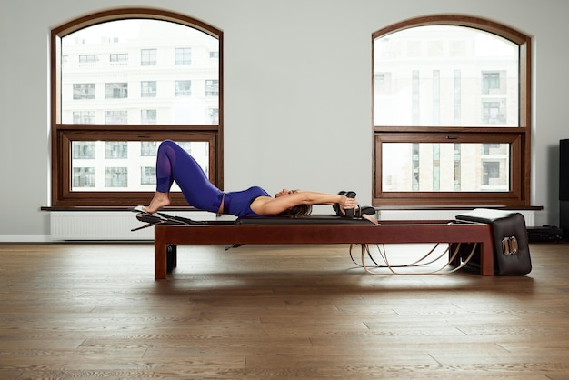 L'instructeur fait des exercices sur le réformateur une belle fille s'entraîne sur le simulateur de réformateur moderne pour travailler les muscles profonds l'équipement de réformateur modernisé pour le Pilates et le yoga