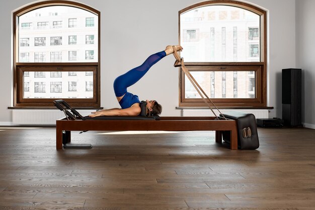 L'instructeur fait des exercices sur le réformateur une belle fille s'entraîne sur le simulateur de réformateur moderne pour travailler les muscles profonds l'équipement de réformateur modernisé pour le Pilates et le yoga