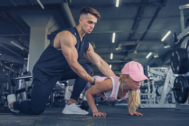 Instructeur de fitness aide une fille à faire des pompes sur la formation dans un centre de remise en forme