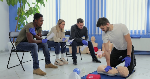 Instructeur d'homme montrant comment faire des compressions thoraciques avec un mannequin pendant la formation de groupe de premiers secours à l'intérieur.