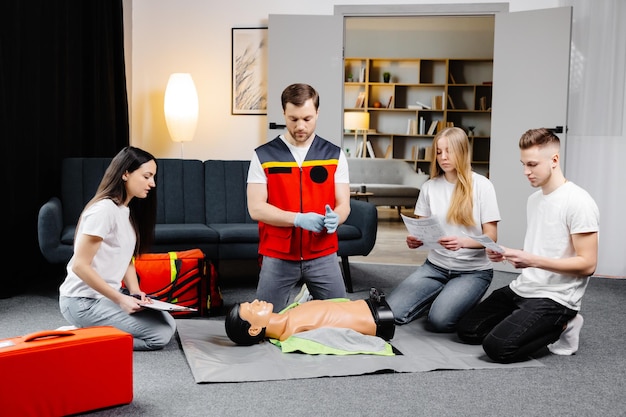 Instructeur de jeune homme aidant à faire des compressions cardiaques de premiers soins avec mannequin pendant la formation de groupe à l'intérieur