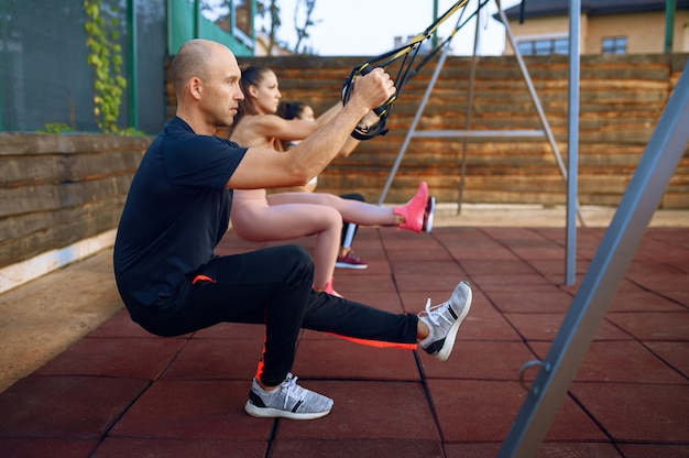 Instructeur masculin et groupe de femmes faisant de l'exercice sur un terrain de sport en plein air, entraînement de remise en forme