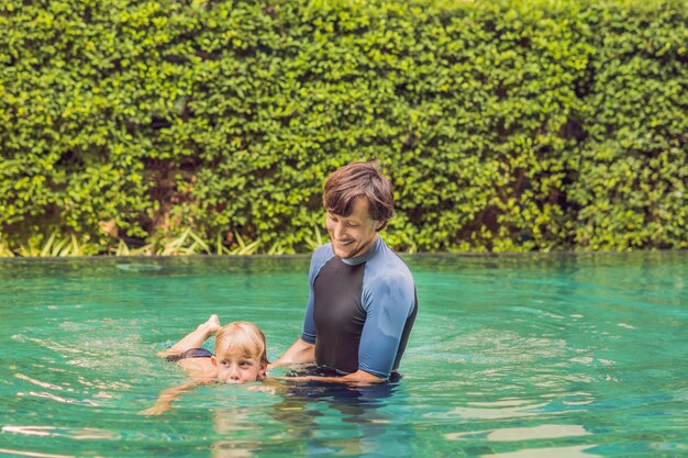 Un instructeur masculin nageant pour les enfants apprend à un garçon heureux à nager dans la piscine