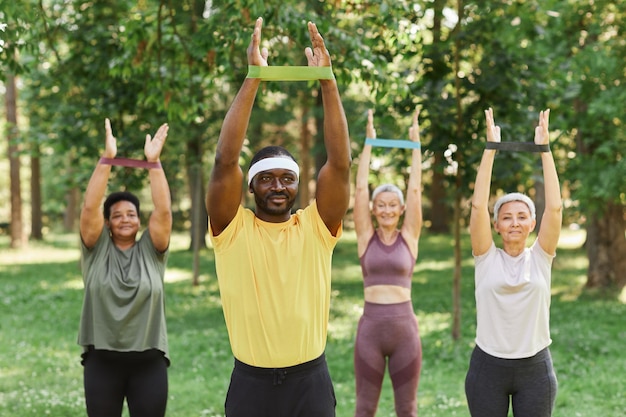 Instructeur de sport masculin dans le parc avec des femmes âgées s'entraînant avec des élastiques