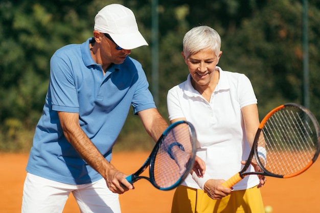 Instructeur de tennis avec une femme âgée sur terre battue Femme ayant une leçon de tennis