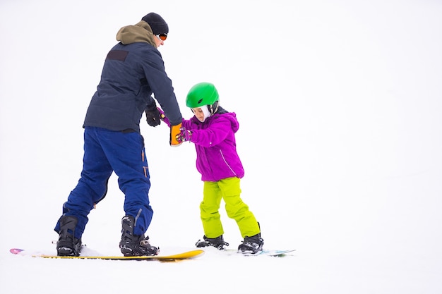 Les instructeurs enseignent à un enfant sur une pente de neige à faire du snowboard