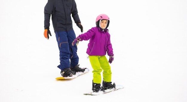 Les instructeurs enseignent à un enfant sur une pente de neige à faire du snowboard