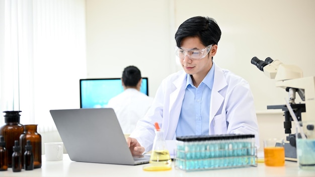 Intelligent et beau jeune scientifique asiatique travaillant dans son bureau à l'aide d'un ordinateur portable