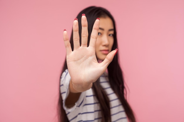 Interdiction, notion d'interdiction. Portrait d'une fille sérieuse aux cheveux bruns tenant la main, montrant Arrêter, bloquer le geste, avertir du danger, refuser de communiquer. tourné en studio isolé sur fond rose