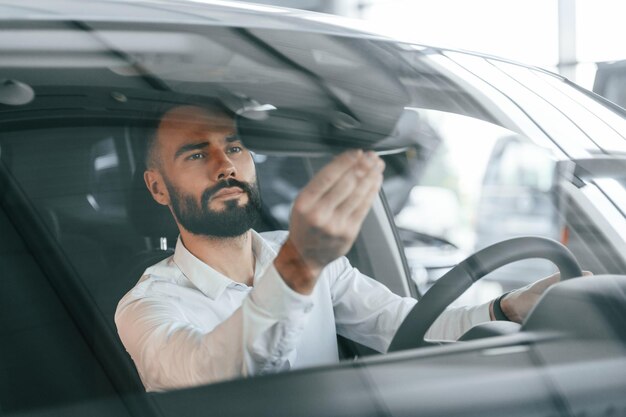 À l'intérieur de l'automobile, un jeune homme en vêtements blancs est chez le concessionnaire automobile