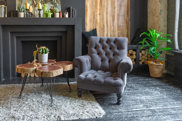 Intérieur brutal sombre du salon décoré de rondins de bois. fauteuils moelleux jaunes et gris, immense baie vitrée et cheminée