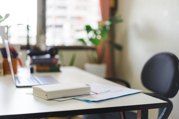 Intérieur avec une chaise devant une table blanche avec un ordinateur portable et des documents sous le bloc-notes