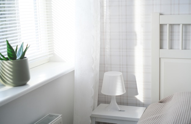 L'intérieur de la chambre dans des tons blancs avec une lampe de table de chevet et une fleur sur le