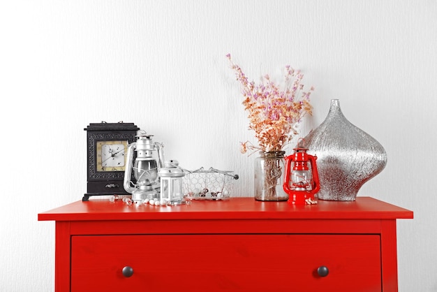 Intérieur de la chambre avec lanternes de commode en bois rouge et horloge sur fond de mur clair