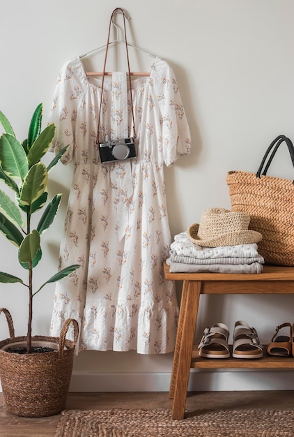 Intérieur de chambre de style confortable une robe sur un cintre sur la caméra murale un banc en chêne avec une pile de vêtements un sac de paille des chaussures Concept de maison confortable Ensemble de vêtements de marche de voyage