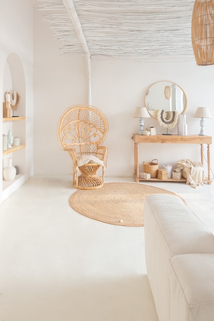 Intérieur confortable d'un appartement lumineux de style balinais avec murs blancs, chaise en bambou, grand canapé blanc et décorations
