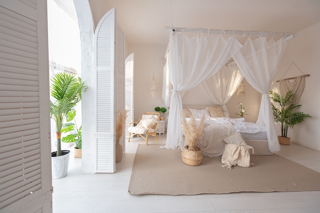 Intérieur confortable d'un appartement lumineux de style balinais avec murs blancs et mobilier en bambou. chambre à coucher avec veilleuses, lit avec balanchin et grandes fenêtres