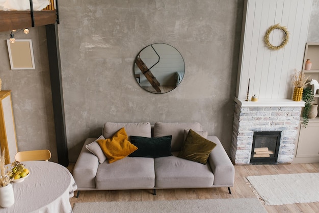 Intérieur confortable de style scandinave d'un salon avec un canapé gris avec des oreillers, une table à manger ronde et une cheminée dans une maison de campagne