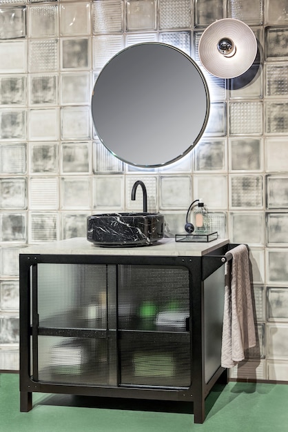 Intérieur contemporain de la salle de bains avec lavabo en marbre noir et miroir rond illuminé accroché au mur carrelé