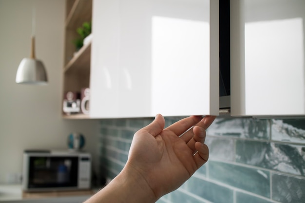 Intérieur de cuisine avec mobilier moderne. L'homme ouvre un meuble suspendu moderne pour une cuisine sans poignées de porte, avec une marge de 2 cm en bas pour les mains