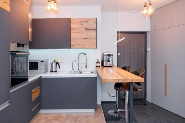 Intérieur De Cuisine Moderne Avec Des Lumières Sur La Table En Bois Marron Et Tabourets De Bar, Machine à Café. Intérieur Contemporain Avec Des éléments De Loft