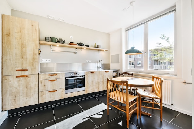 Intérieur de cuisine moderne et lumineuse. Table ronde en bois avec des chaises situées sous la lampe près de l'étagère avec de la vaisselle dans la salle à manger lumineuse pendant la journée