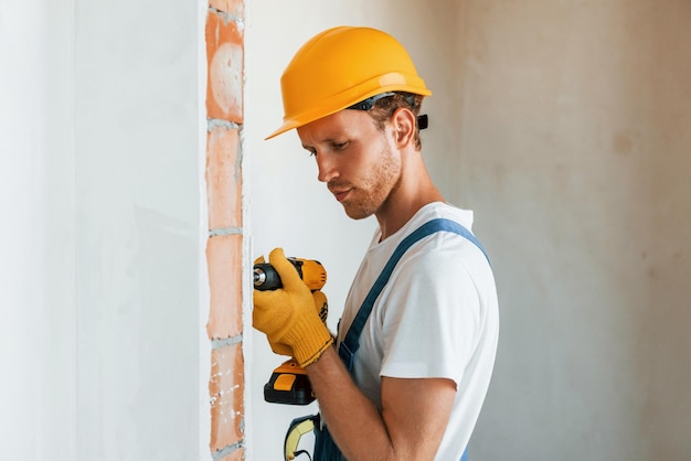 À l'intérieur dans une salle inachevée Jeune homme travaillant en uniforme à la construction pendant la journée