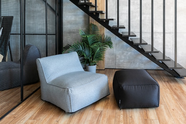 Intérieur du jeune studio de style loft avec des meubles moelleux au premier plan, escalier métallique et armoire en arrière-plan