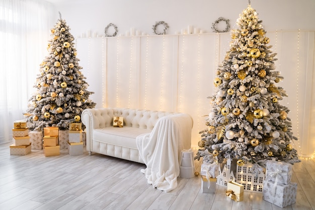 Intérieur du salon blanc avec des arbres du nouvel an décorés de boîtes à cadeaux et d'un canapé blanc de couleur dorée