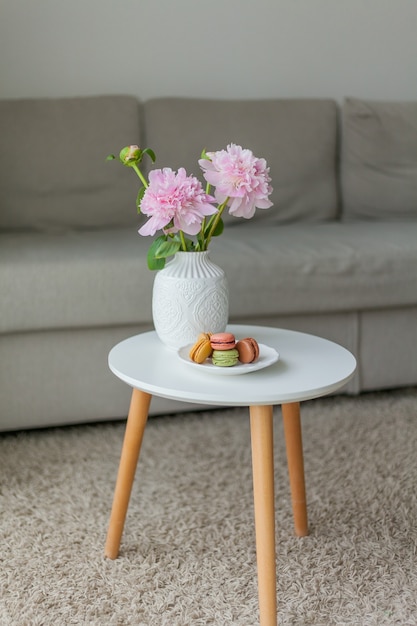 Intérieur du salon. Bouquet de pivoines roses dans un vase, pâtisseries de macarons français multicolores. Confortable. Printemps.