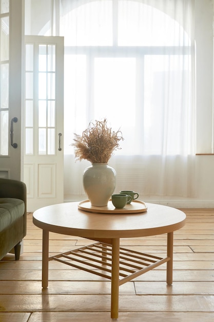 Intérieur du salon moderne décoré d'un vase de bouquet de fleurs placé sur une table en bois de forme ronde dans un appartement