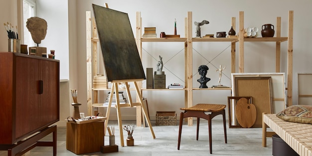 Photo intérieur d'espace de travail d'artiste unique avec une élégante commode en teck, un chevalet en bois, une bibliothèque, des œuvres d'art, des accessoires de peinture, une décoration et des objets personnels élégants. salle de travail moderne pour artiste modèle