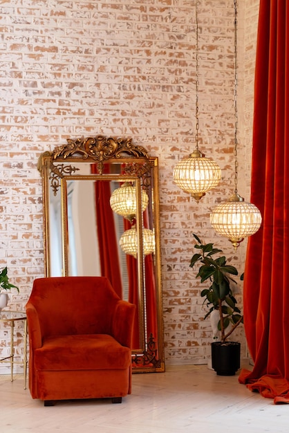 Un intérieur français moderne avec des rideaux bordeaux en velours côtelé, un fauteuil, un miroir doré vintage et des lustres en cristal contre un mur de briques. Mise au point sélective douce.