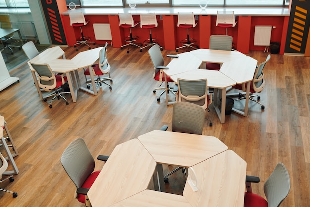 Photo intérieur d'un grand bureau à aire ouverte avec de nombreuses chaises par différents types de tables contre zone de repos avec canapé et coussins sans personne autour