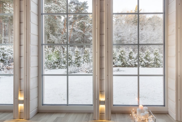 Intérieur lumineux de la chambre dans maison en bois avec une grande fenêtre donnant sur la cour d'hiver. Paysage d'hiver enneigé dans la fenêtre blanche. Maison et jardin, concept de Noël.